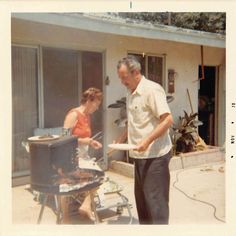 an old man and woman grilling food on the back deck of a house,