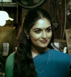 a woman with long dark hair wearing a blue blouse and green top smiling at the camera