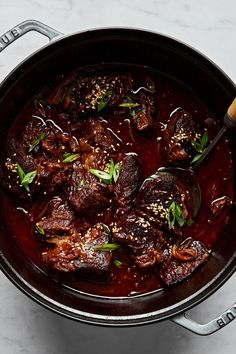 a pot filled with meat and sauce on top of a white countertop next to a wooden spoon