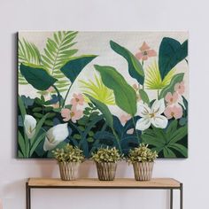 three potted plants sit on a table in front of a painting with tropical leaves and flowers