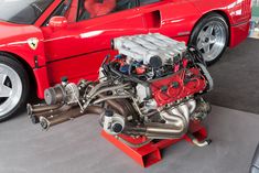 a red sports car parked in a garage with its engine on the ground next to it