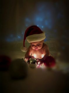 a baby wearing a santa hat playing with a christmas ornament in the dark