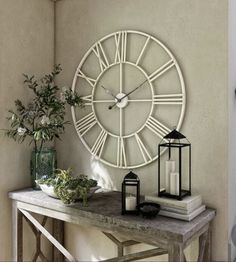 a large white clock mounted to the side of a wall next to a table with flowers and candles