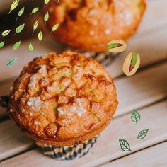 two muffins sitting on top of a wooden table next to nuts and leaves