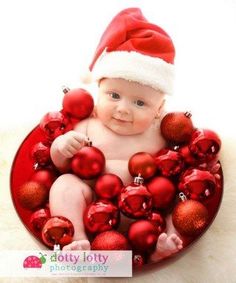 a baby wearing a santa hat sitting in a bowl filled with christmas ornaments