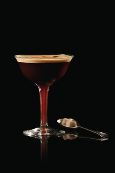 a glass filled with liquid sitting on top of a table next to two spoons