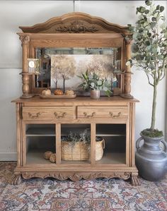 a wooden dresser with an ornate mirror and potted plant on top in front of it