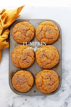 pumpkin muffins in a baking pan on a marble counter top with a yellow napkin