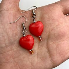 pair of red heart shaped earrings with silver earwires held in the palm of someone's hand