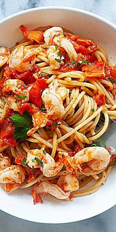 pasta with shrimp and tomato sauce in a white bowl on a marble countertop, ready to be eaten