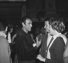 black and white photograph of two people talking to each other at a party with others