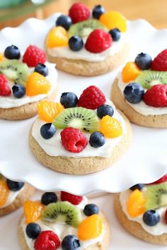 fruit topped cookies are arranged on a white platter with berries, kiwis and oranges