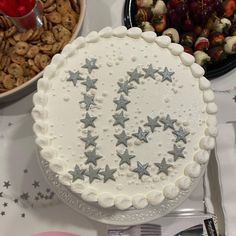 a white cake with silver stars on it sitting in front of a bowl of fruit