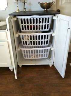 a white cabinet filled with laundry baskets next to a sink