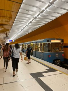 several people are walking along the platform near a subway train that is pulling into the station