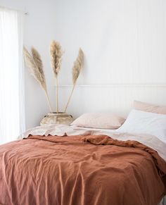 the bed is made and has two tall plants on it's headboard, along with an orange comforter