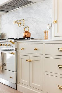 a kitchen with white cabinets and gold knobs on the stove top, along with an oven