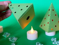 someone is holding a lit candle in front of two paper christmas trees with holes on them