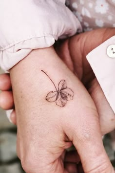 two hands holding each other with a small flower tattoo on the left hand and an arrow in the middle