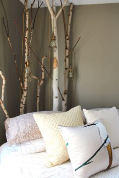 a bed topped with lots of pillows next to white birch trees in a room filled with gray walls