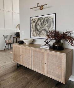 a living room with a large painting on the wall next to a wooden cabinet and chair