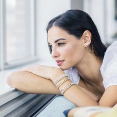 a woman leaning on a window sill wearing bracelets