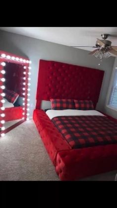 a bedroom with a large red bed and lighted mirror in the corner, along with a ceiling fan