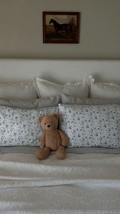 a brown teddy bear sitting on top of a bed next to pillows and pillow cases