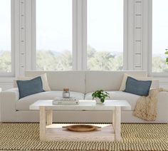 a living room with white couches and blue throw pillows on the coffee table in front of large windows