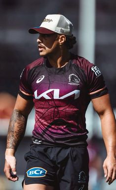 a rugby player wearing a maroon jersey and black shorts is looking to the side with his hand on his hip