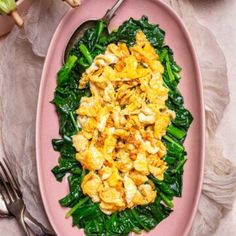 a pink plate topped with eggs and greens next to two silverware on a table