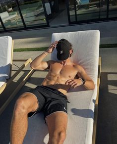 a man laying on top of a white couch next to a glass building and wearing a black hat