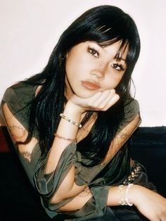 a woman sitting on top of a black couch next to a white wall with her hand under her chin