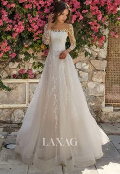 a woman standing in front of flowers wearing a wedding dress with long sleeves and off the shoulder