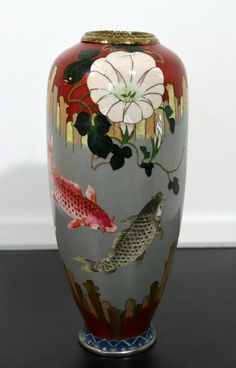 a vase with fish and flowers painted on the side, sitting on a black surface