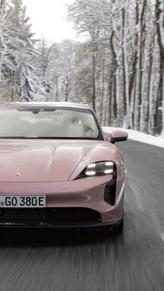 a pink sports car driving down the road in front of trees and snow covered ground