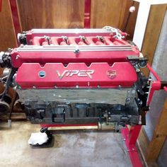 a red engine sitting on top of a metal stand next to a wooden wall and floor