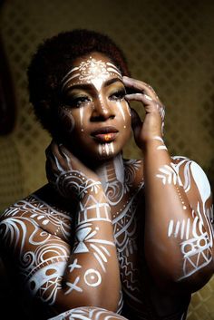 a woman with white paint on her body and hands behind her head, holding her hand to her face