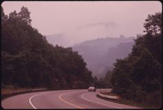 a car is driving down the road on a foggy day with mountains in the background