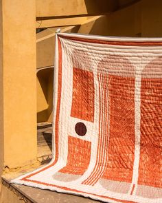 an orange and white quilt hanging on the side of a building with a black dot