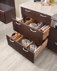 an open drawer with pots and pans in it on the floor next to a counter