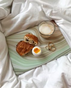 a breakfast tray with an egg, croissants and coffee on the bed