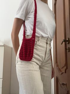 a woman in white shirt holding a red crocheted bag over her shoulder while standing next to a door