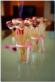 there are many cupcakes in the glass vase on the table with pink ribbons