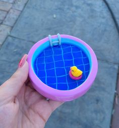 a hand holding a plastic toy with a yellow rubber duck in it's pool