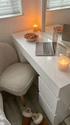 a laptop computer sitting on top of a white desk next to a candle and a bowl of food