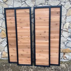 two wooden doors sitting next to each other near a stone wall with black trim around the edges