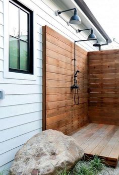 an outdoor shower with wooden planks next to a rock and planter on the side of a house