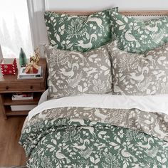 a bed covered in green and white comforter next to a night stand with christmas decorations on it