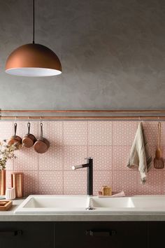 a kitchen with pink tiles on the wall and copper lighting fixture above it, next to a sink